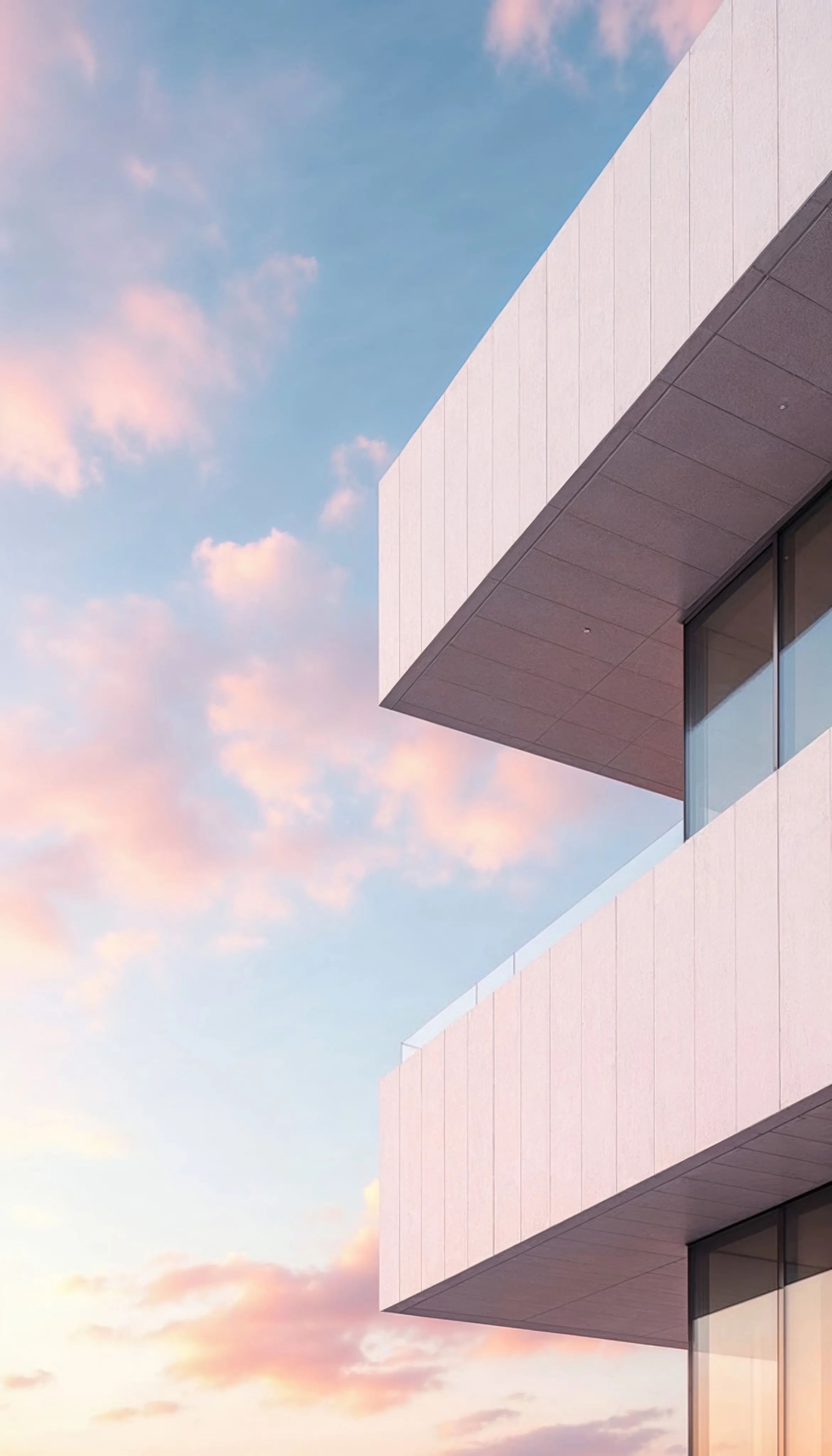 Corner of a modern concrete building with cantilevered floors against a pastel pink and blue sunset sky